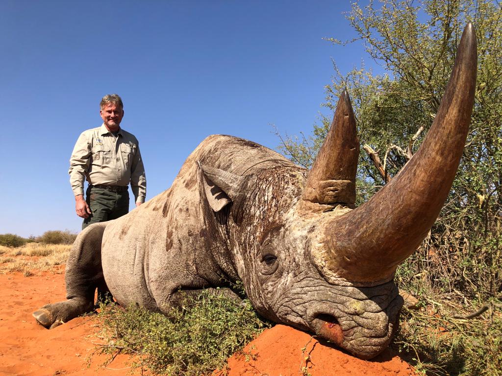 Hunter standing beside a rhino trophy on red sand